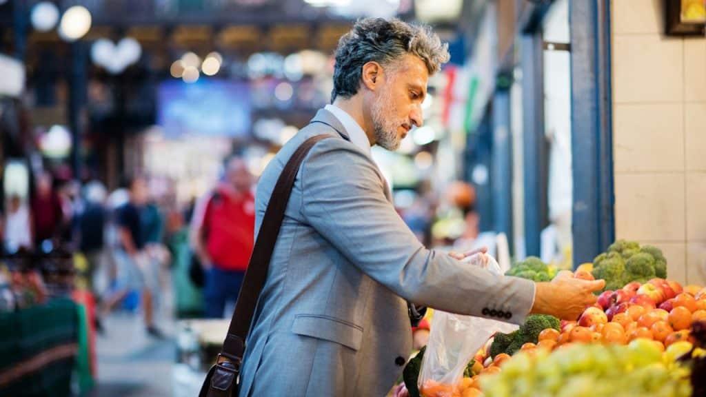 A handsome man is buying fruit from a vendor with a blurred background.
