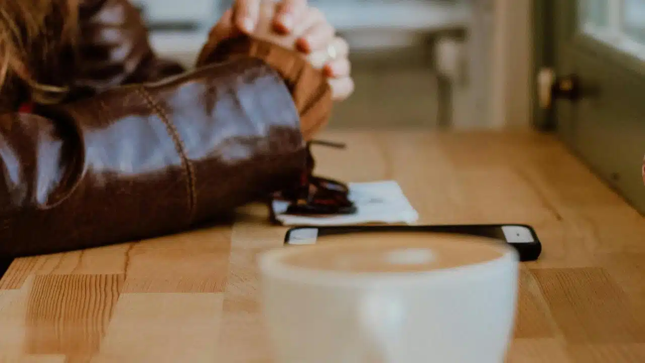 A person sitting at a cafΓ© table with a coffee cup