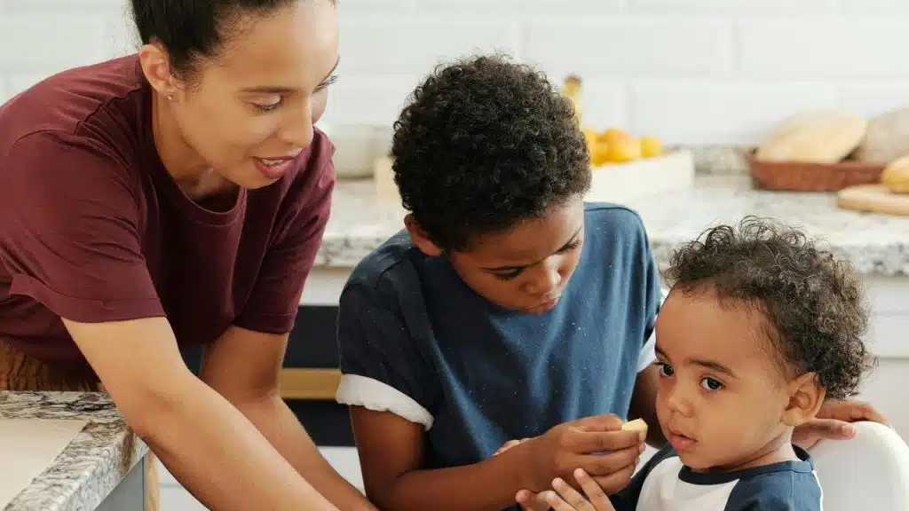A woman helping two young children in a kitchen.