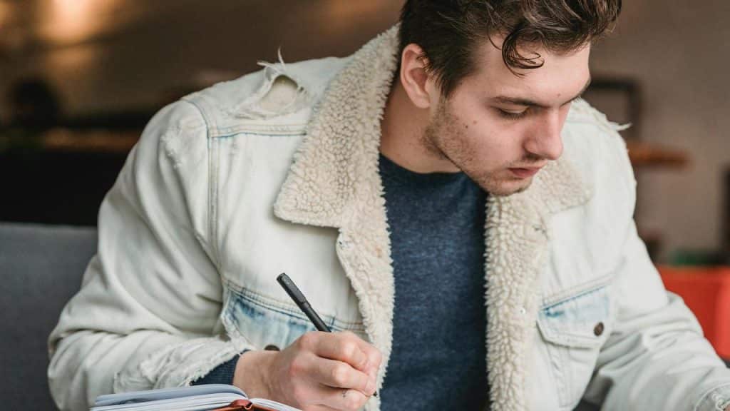 A man writing in a notebook while sitting at a table.