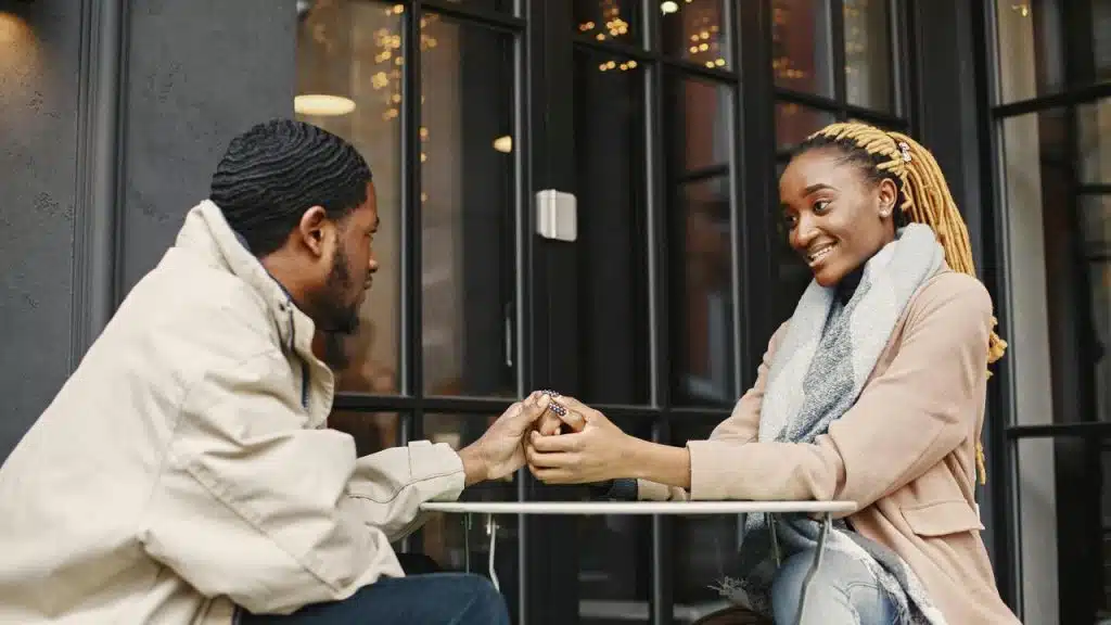 A man placing a ring on a woman’s finger at an outdoor table.
