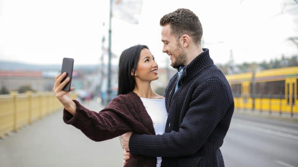 A man and woman smiling at each other while the woman holds up a smartphone.