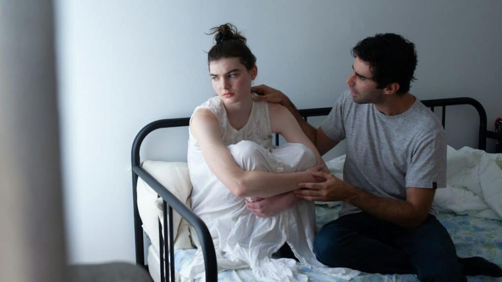 A man reaches out to a woman who is sitting curled up and looking away.