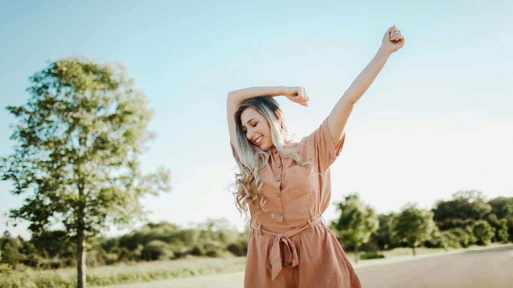 A woman stretching her arms happily outdoors on a sunny day.