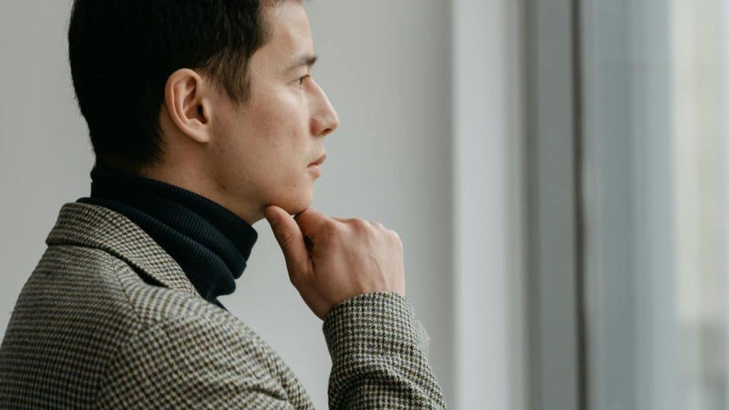 A man looking out a window while resting his chin on his hand