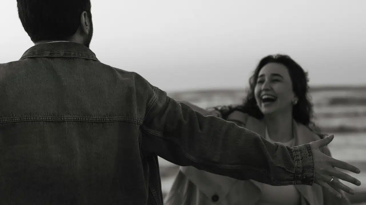 A man with open hands standing in front of a laughing woman who is coming towards him.