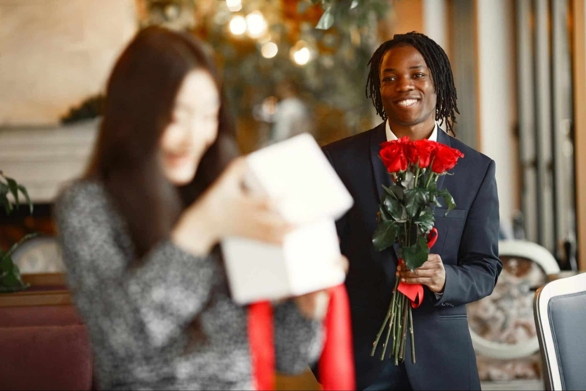 A man holding a bunch of roses behind a woman.