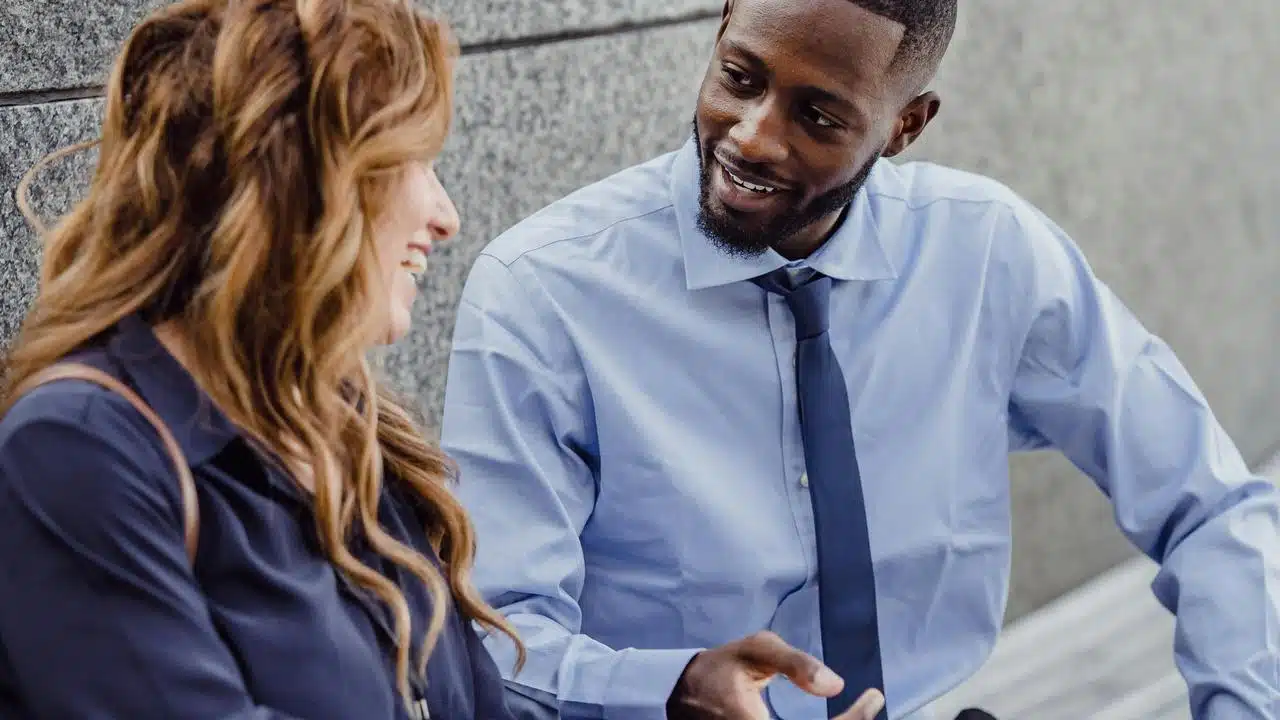 A man and woman smiling and talking outdoors.