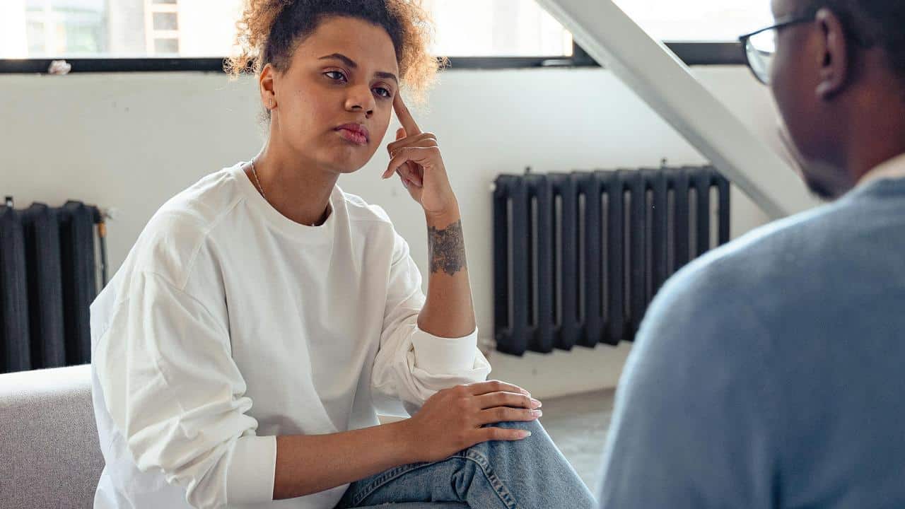 A woman listening thoughtfully to another person during a conversation indoors.