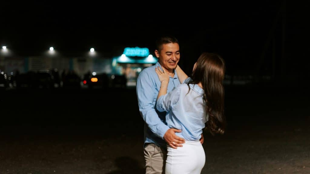 A man and a woman are standing in a parking lot at night.