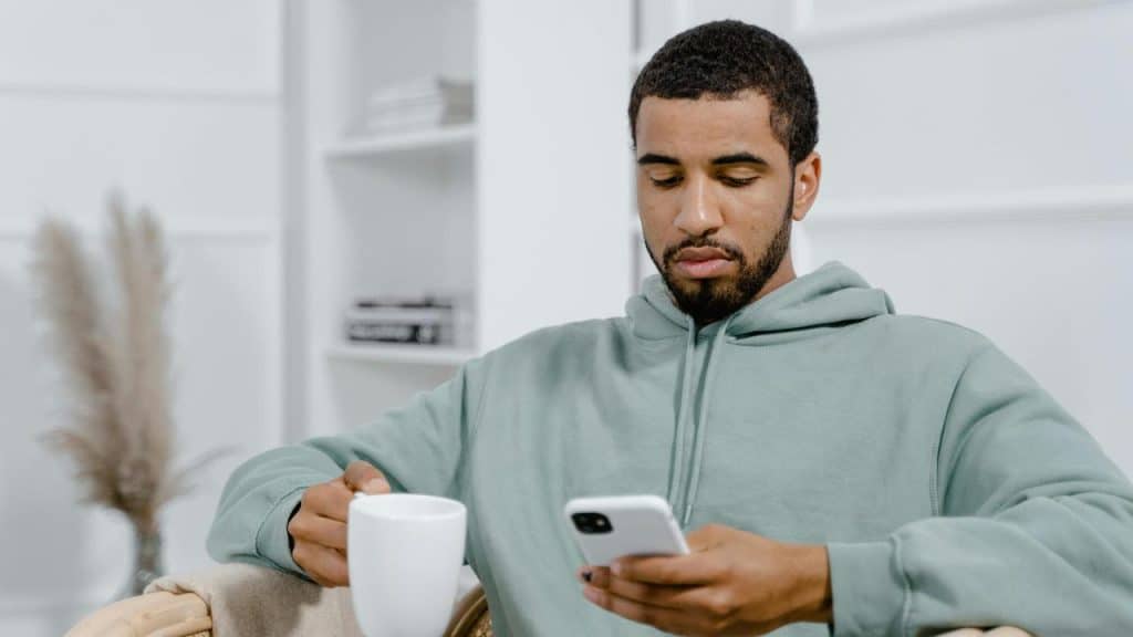A man holding a mug while looking at his phone.
