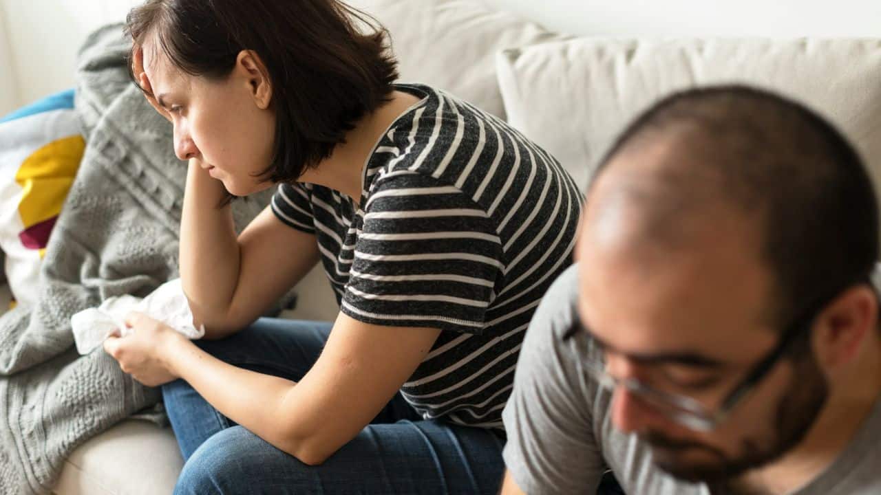 A woman in a striped shirt sits on a couch while a man sits nearby.