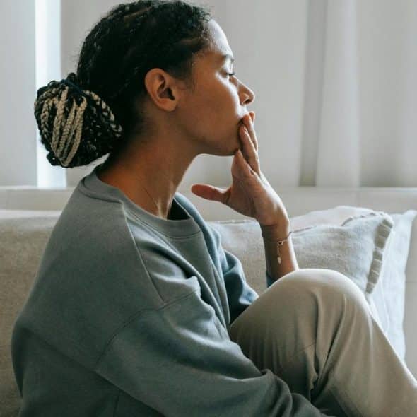 A woman sitting on a couch, looking thoughtful with her hand on her chin.