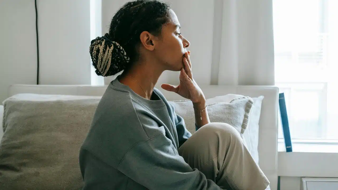 A woman sitting on a couch, looking thoughtful with her hand on her chin.