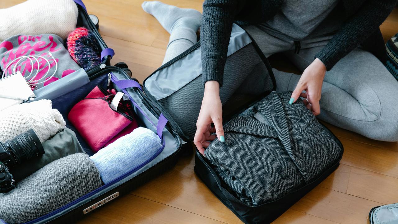 A person packing clothes and items into an open suitcase on the floor.