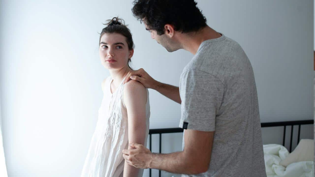 A man holding her wife’s shoulder from the backside.