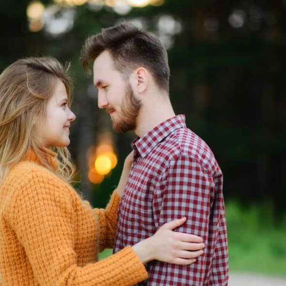 A man and woman facing each other while standing near a green field.