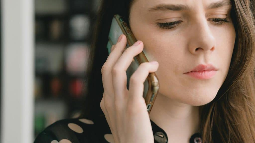 A woman holding a smartphone to her ear with a concerned expression.
