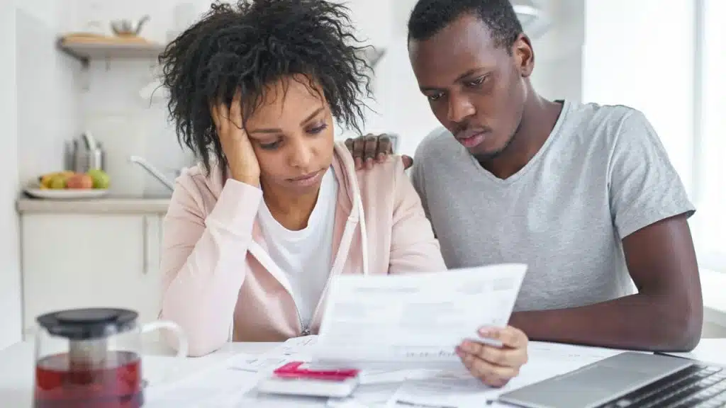 A man and woman look at a paper document while sitting at a kitchen table.