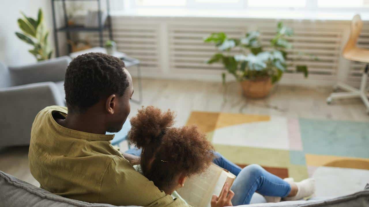 A parent and child sitting together on a couch, reading a book at home.
