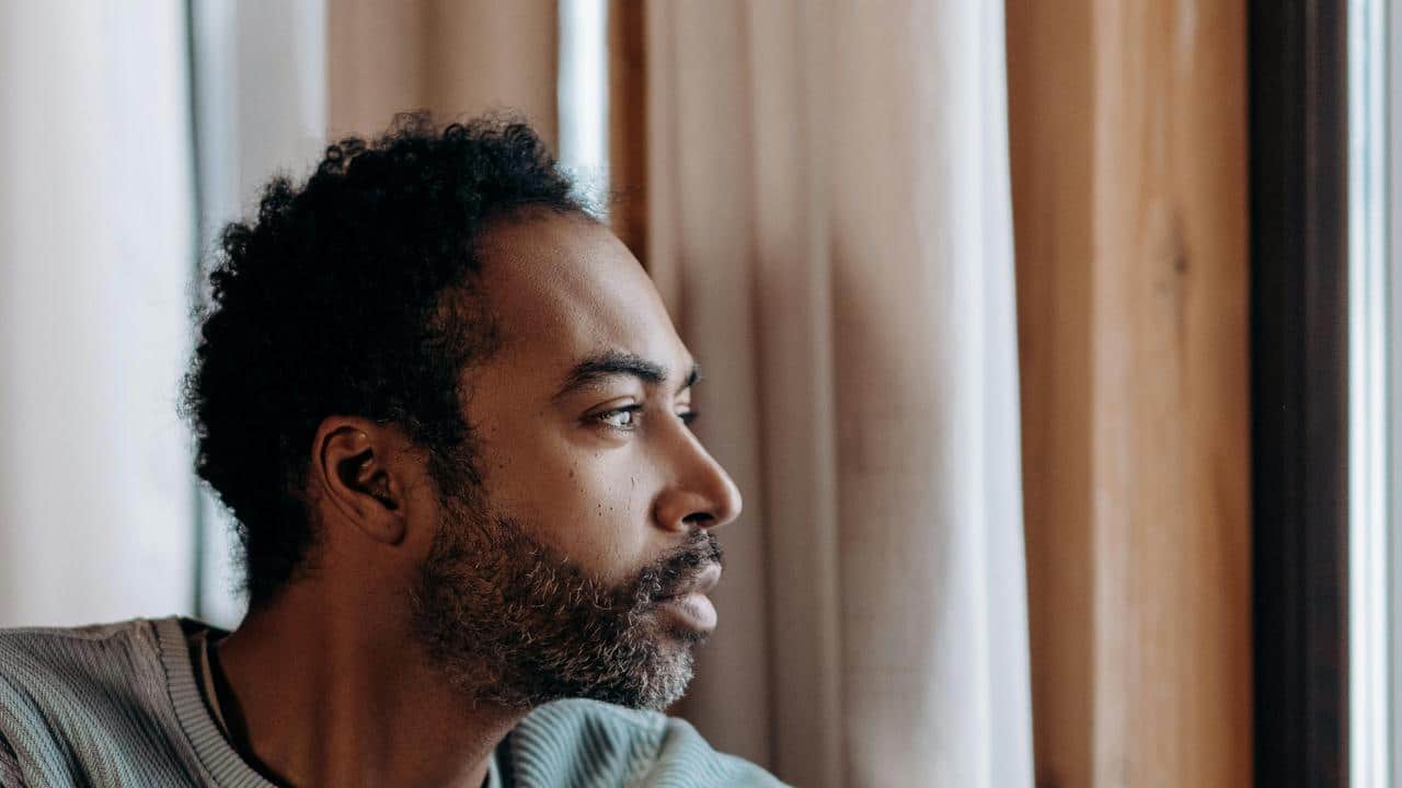 A person looking out a window indoors with a thoughtful expression.
