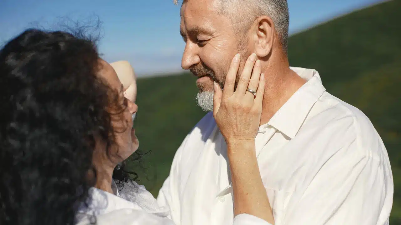 A couple smiling at each other while gently touching faces outdoors.