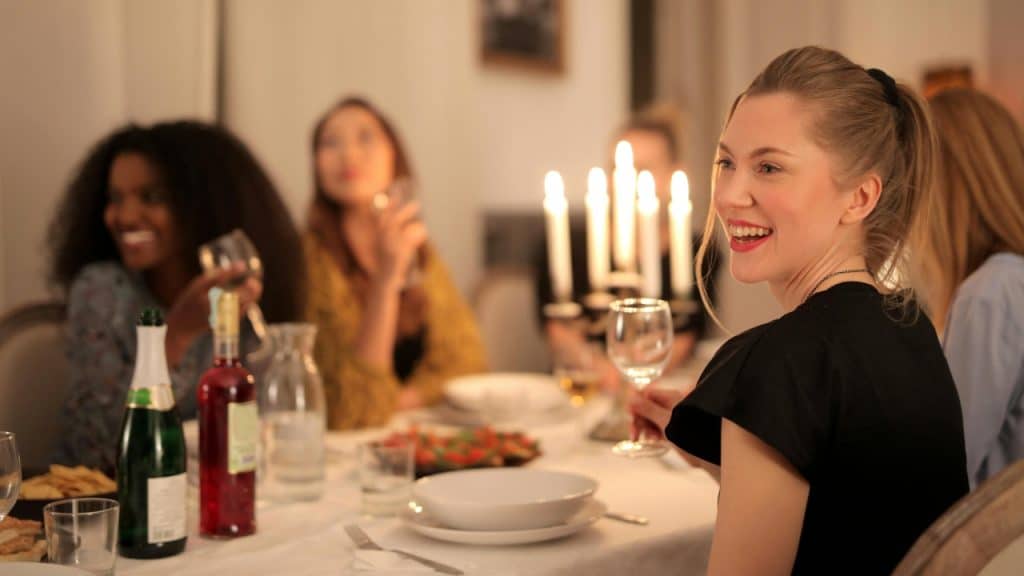 A group of friends sits at a long dinner table with candles and wine.