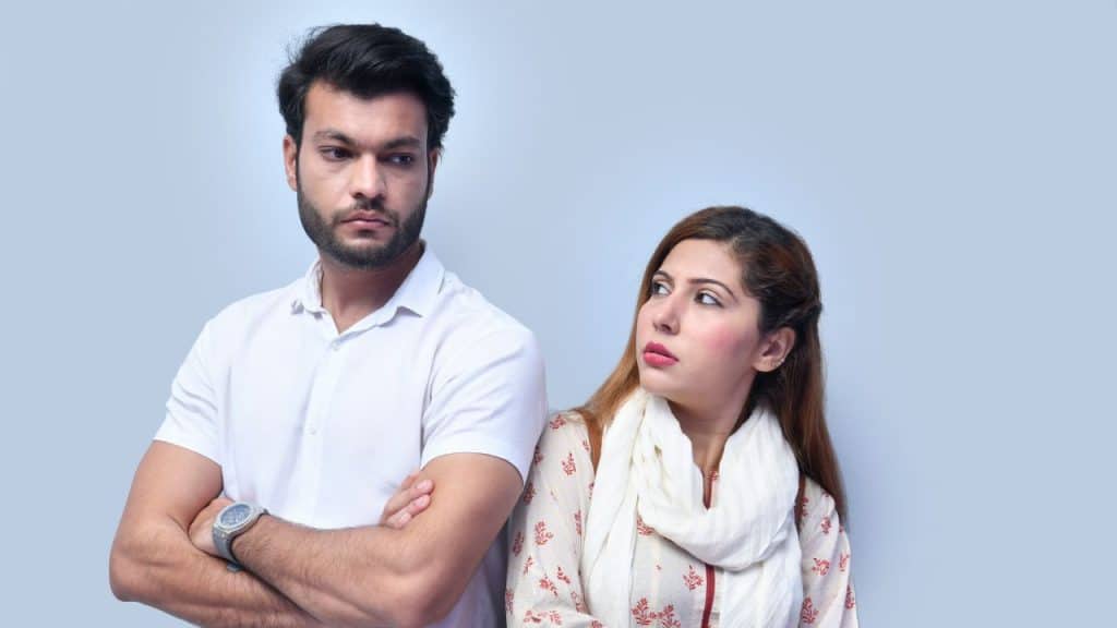 A woman looks toward a man with his arms crossed facing away from her.