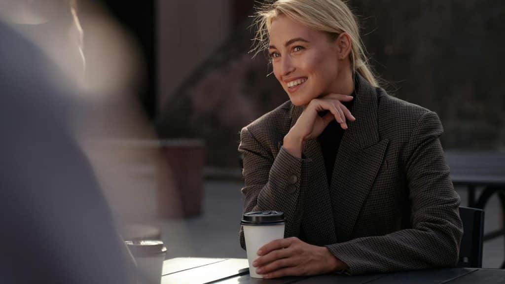 A smiling woman at an outdoor café holding a coffee cup.