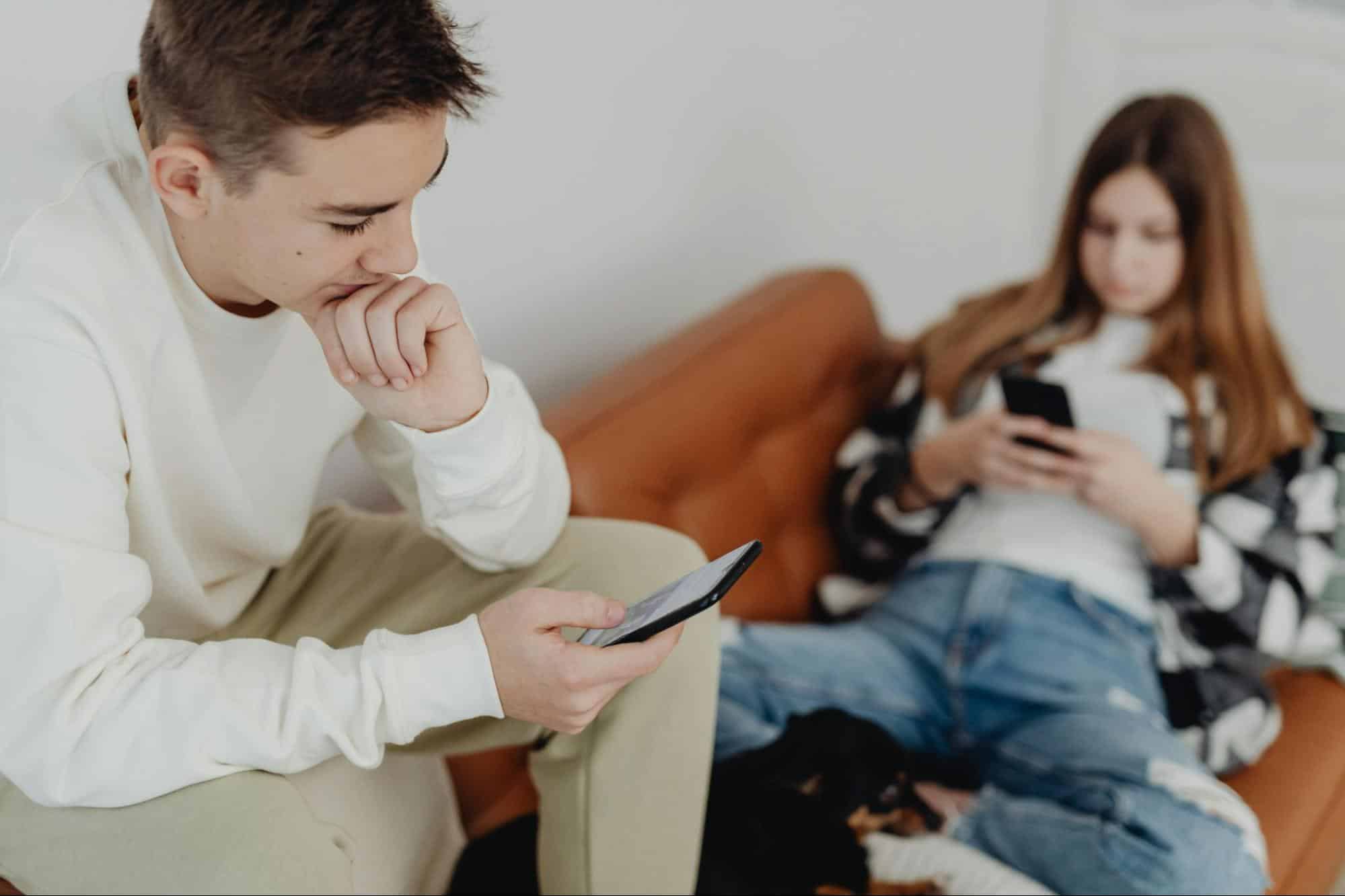 A couple sitting on a couch using their phones.