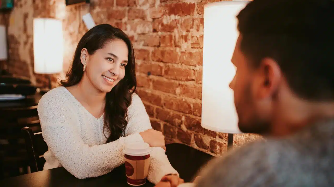 A woman smiling at a man across a table in a café.