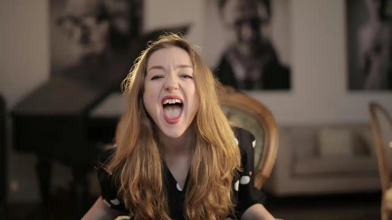 A woman with long hair leaning forward, mouth wide open in a living room.