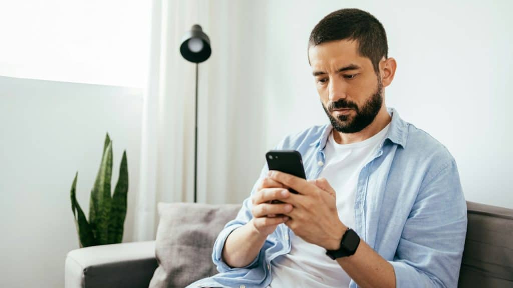 A man with a beard is reading a text message on his cell phone.