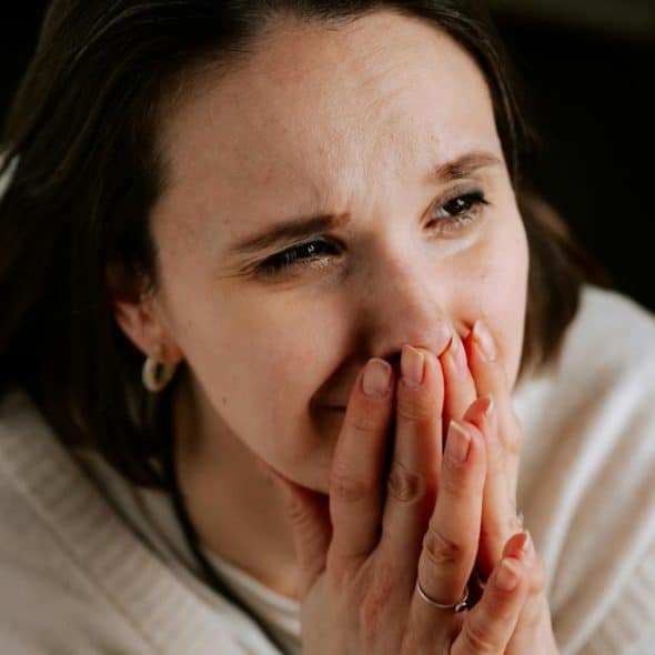 A woman holding her hands over her mouth with an emotional expression.