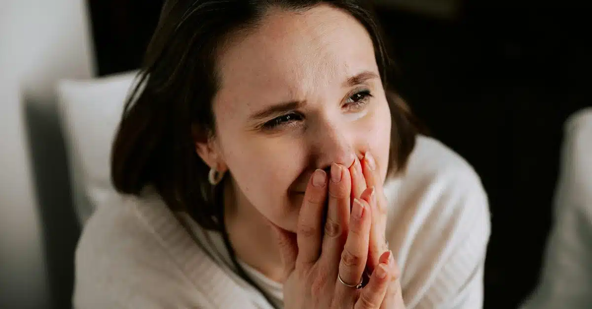 A woman holding her hands over her mouth with an emotional expression.