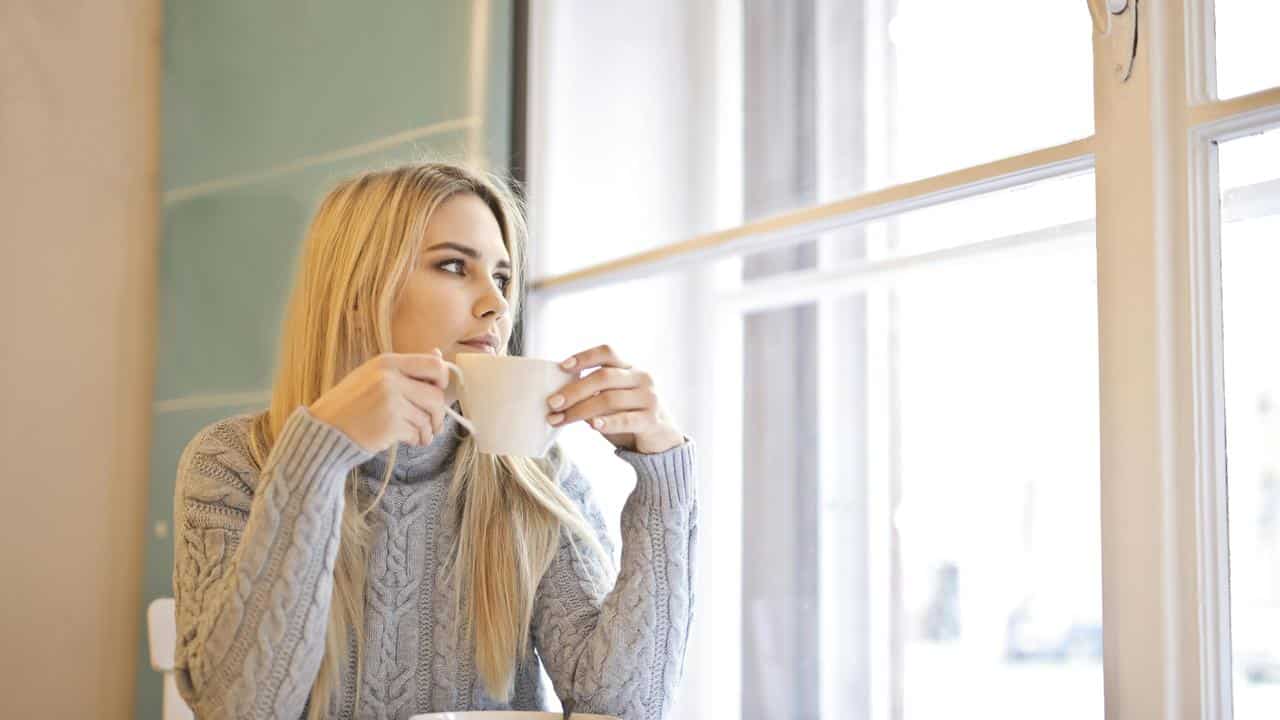 A woman holding a cup and looking out a window.