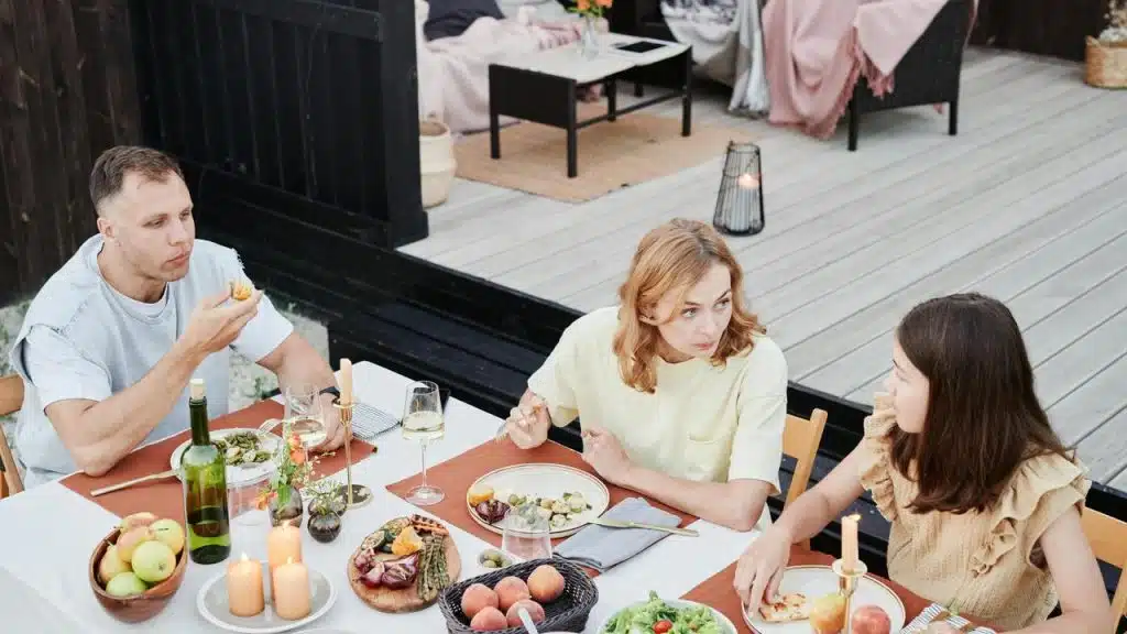 A family sitting outdoors at a table, eating and talking during a meal.