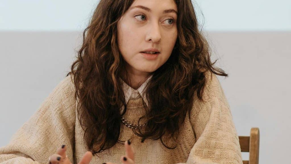 A woman with curly hair speaking while seated at a table.