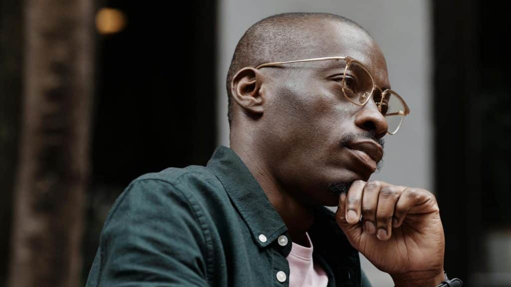 A man wearing glasses resting his chin on his hand, looking thoughtful.