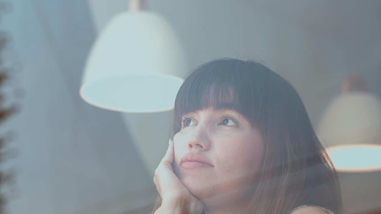 A woman resting her face on her hand, gazing upward thoughtfully.