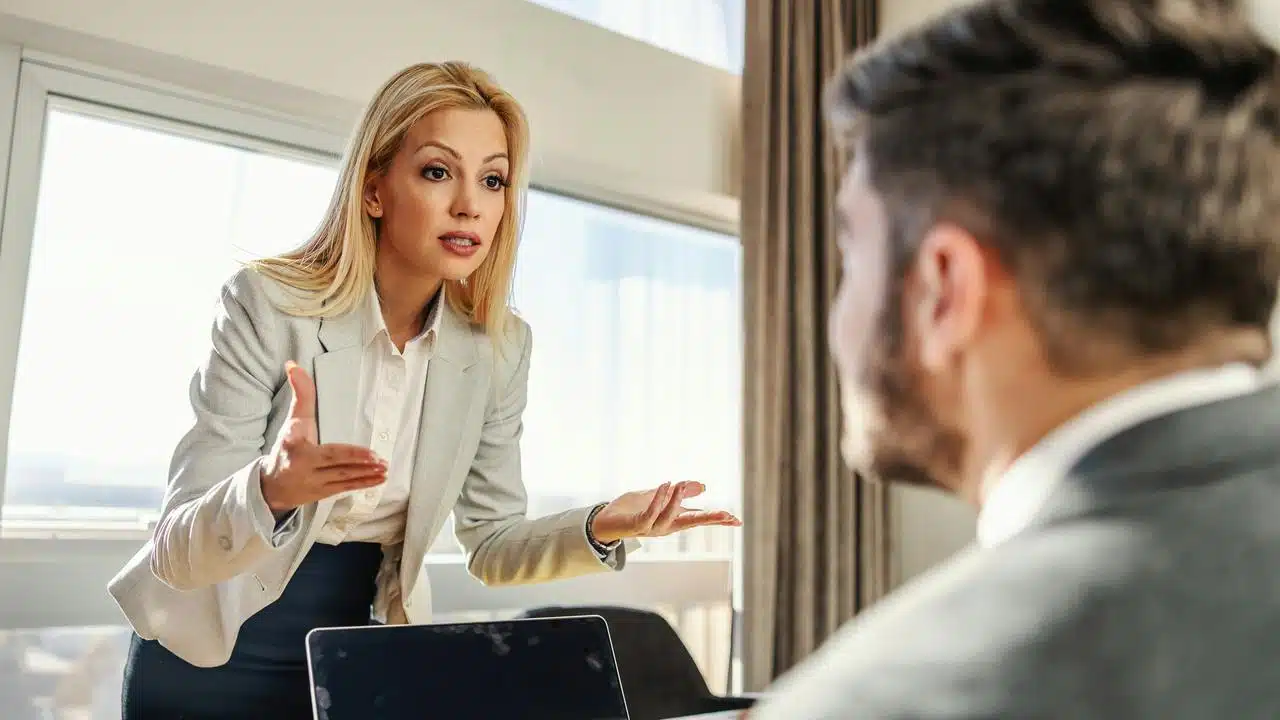 A businesswoman gesturing while speaking to a colleague across a desk.