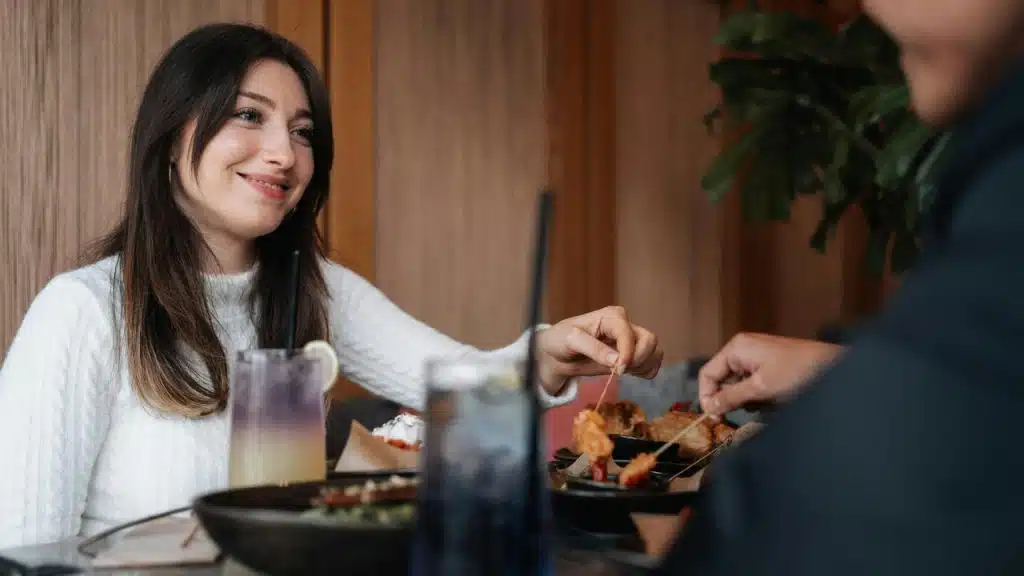 A smiling woman enjoying a meal and drinks while dining with another person at a restaurant.