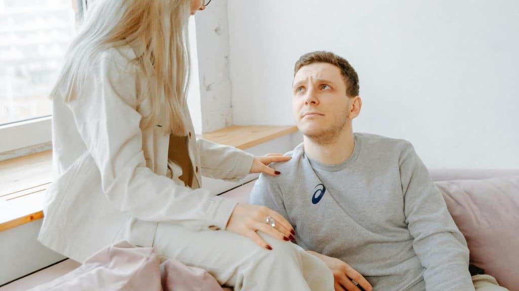 A woman placing a comforting hand on a man’s shoulder while talking to him.