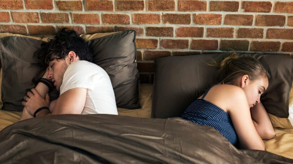 A man and a woman sleep in a bed facing away from each other.