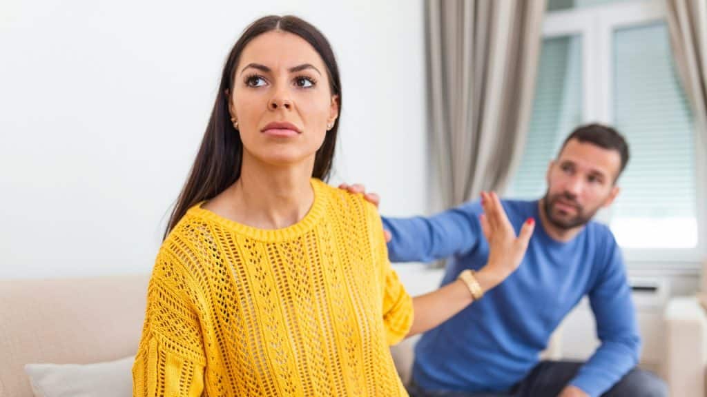 A woman in a yellow sweater holds her hand up to a man behind her.
