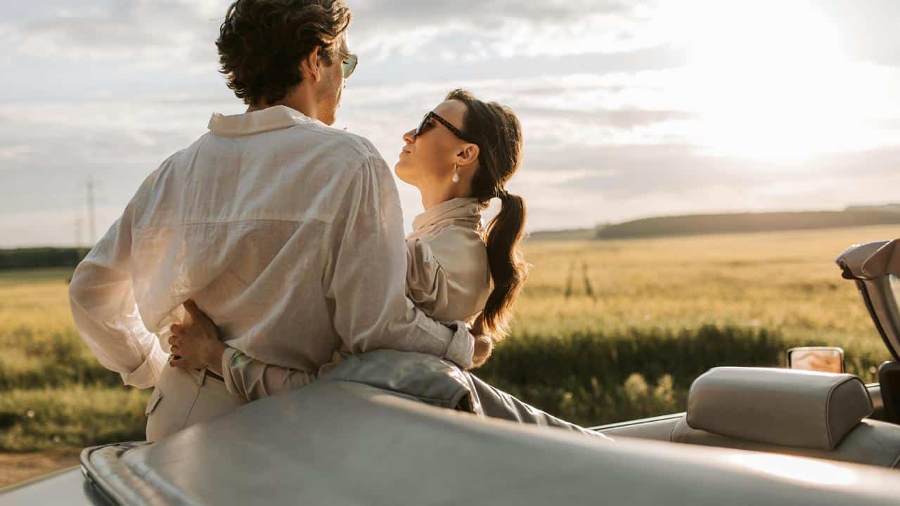 A couple embracing beside a car in a sunny field.