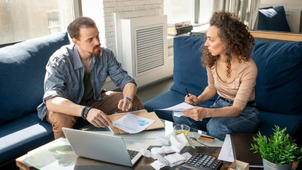 A man and woman sitting on blue sofas discussing papers spread across a coffee table.