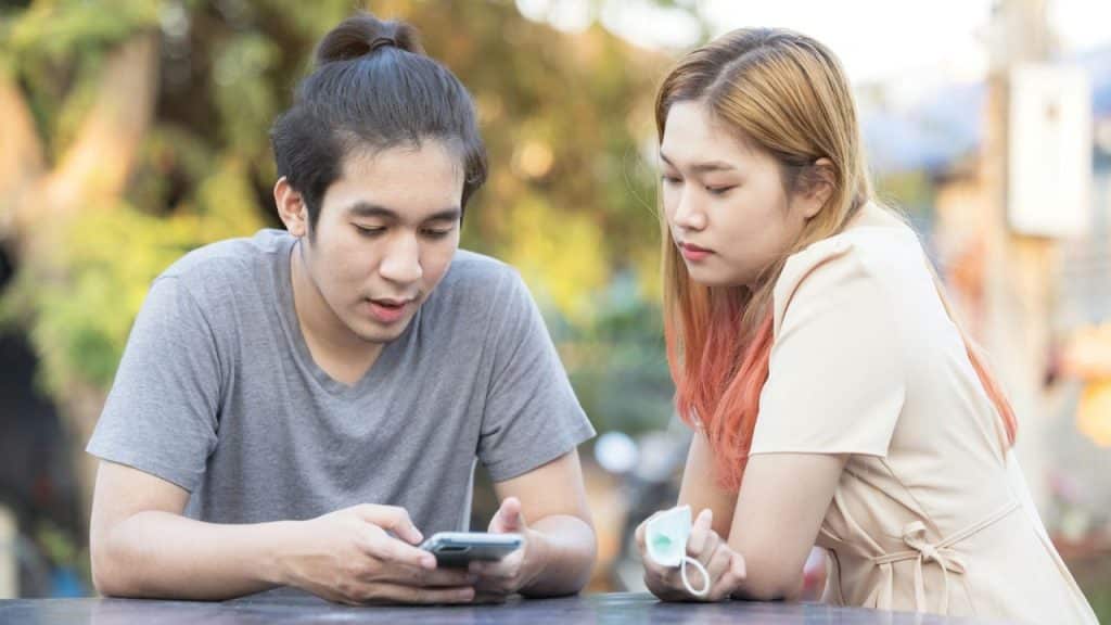 A man looks at a smartphone while a woman sits beside him, looking down at it.
