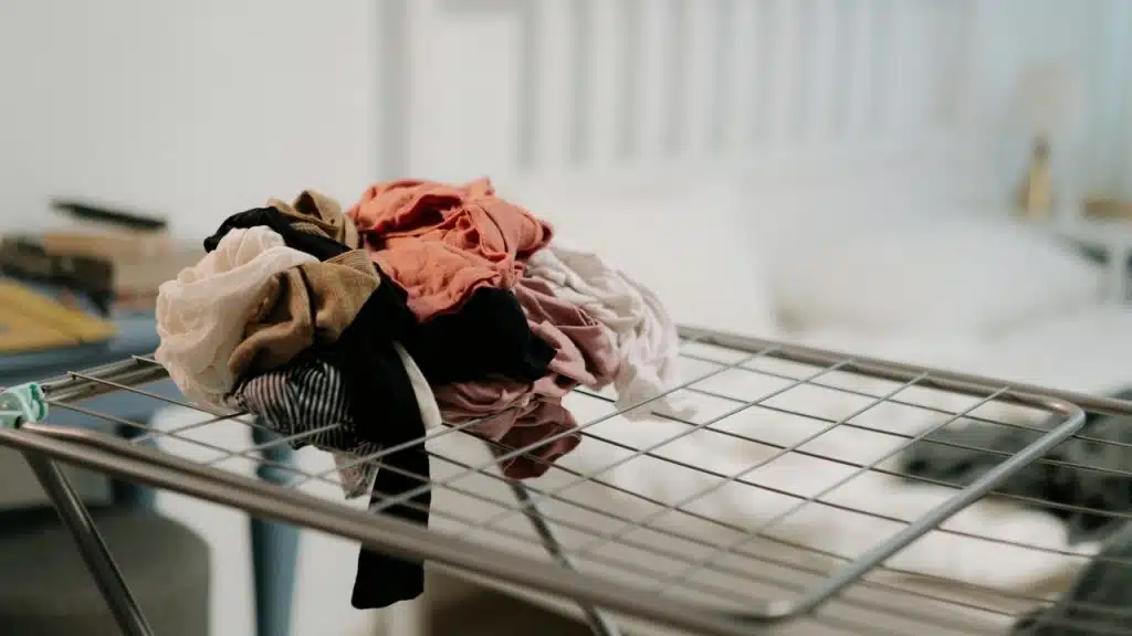 A pile of folded and unfolded colorful laundry sits on a metal drying rack indoors.