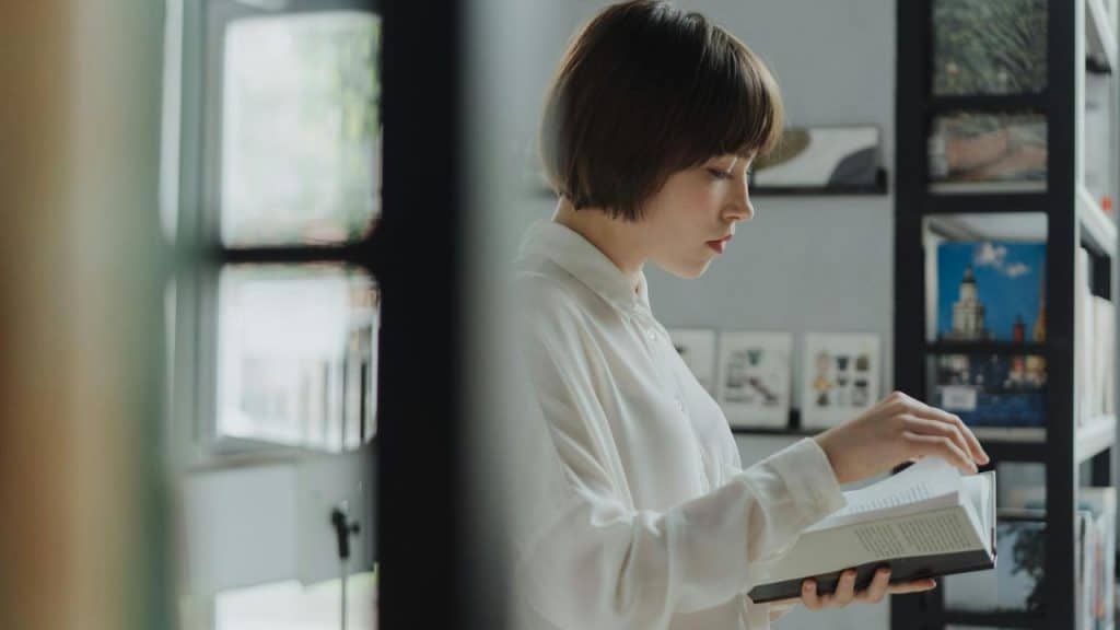 A woman reading a book indoors by a window.